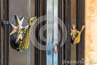 Closeup of brass vintage knockers as dolphin with a trident-shaped tails and Maltese cross at black wooden door Stock Photo
