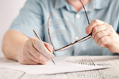 Closeup of businessman hands writing something on piece of paper and holding pair of glasses Stock Photo