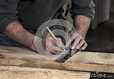 Closeup of carpenter`s rough rugged hands using a pencil and old square to mark a line on wood board to cut Stock Photo