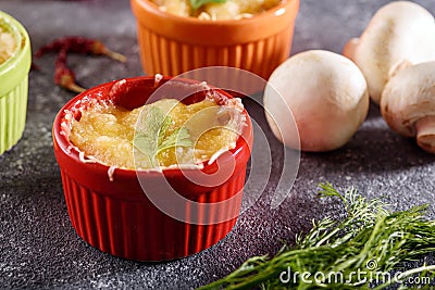 Closeup casserole with mushrooms under cheese crust in multicolored cocoanuts on gray background Stock Photo