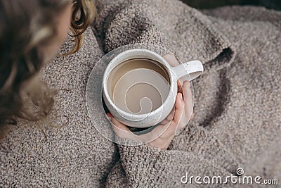 Closeup of caucasian girl, child in beige knitted sweater holding white ceramic spotted cup of coffee. Autumn cozy Stock Photo