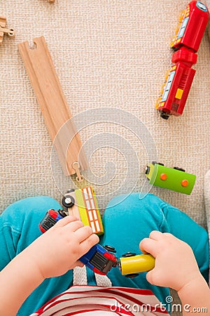 Closeup of child`s hands playing with wooden train toys and railway. Top view. Toddler boy sitting and playing with railroad indo Stock Photo