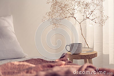 Closeup of coffee cup and flower in glass vase on the bedside table of bright bedroom interior Stock Photo