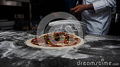 Closeup of a cook taking a whole raw pizza with a peel in the kitchen Stock Photo