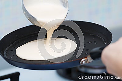 Closeup cooking pancakes on a gas stove. On a hot skillet liquid dough from the ladle is poured Stock Photo