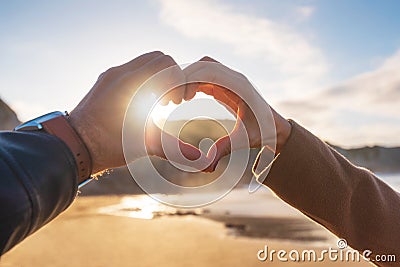 Closeup of couple hands making heart shape in the beach, in autumn season. Happy couple in love. Stock Photo