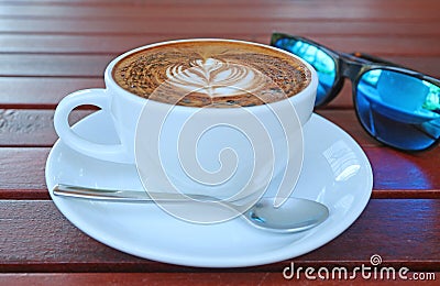 Cup of Hot Cappuccino Coffee with Blurry Sunglasses in Background Stock Photo