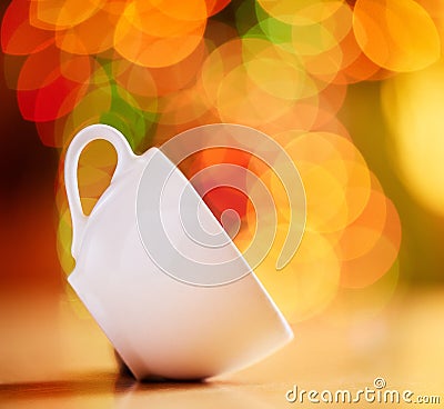 Closeup of a cup isolated against a colourful bokeh background. White teacup tilted on the side on a table. Crockery to Stock Photo