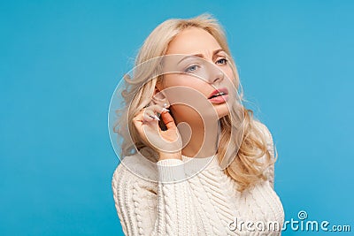 Closeup curious nosy blond woman in white sweater holding hand near ear trying to hear secret information, overhearing private Stock Photo