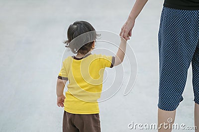 Closeup cute asian kid walk in the hand of parent on concrete floor textured background Stock Photo