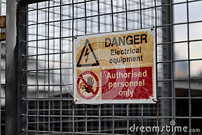 Closeup of a DANGER Electrical equipment sign written on a metal attached to a fence Stock Photo