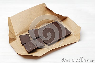 Closeup dark chocolate bar broken into pieces in an open craft paper package Stock Photo