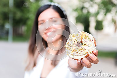 Closeup of delicious and colorful donut in hand of a woman defocused in city park. junk sweet and tasty fast food dessert Stock Photo