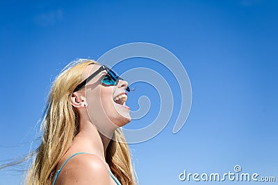 Closeup of delighted happy young blond pretty lady in sunglasses over blue sky on summer day outdoors Stock Photo