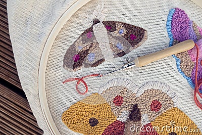 Closeup of embroidered butterflies on two-thread cloth in a hoop with punch needle and brick-red thread inside of it. Punch needle Stock Photo
