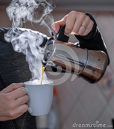 Closeup of female adult hands pouring hot coffee in a white cup from metal coffee pot Stock Photo