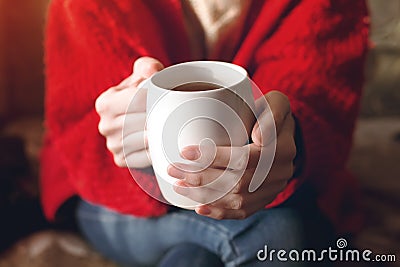 Closeup of female hands with a cup of beverage. Beautiful girl in red sweater holding cup of tea in the morning sunlight Stock Photo
