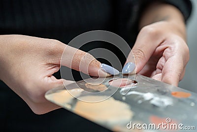 Closeup of female makeup artist holding a used stainless steel makeup mixing palette Stock Photo