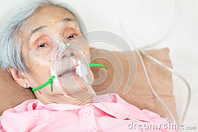 Closeup of female senior patient putting inhalation or oxygen mask in hospital bed or home,sick elderly asian woman undergoing Stock Photo