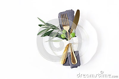 Closeup of festive table summer setting with golden cutlery, olive branch, grey linen napkin, porcelain dinner plate and Stock Photo