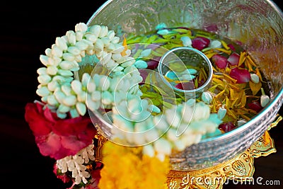 Closeup flower garlands hanging on the edge of silver bowl with flower petal floating on the water in background Stock Photo