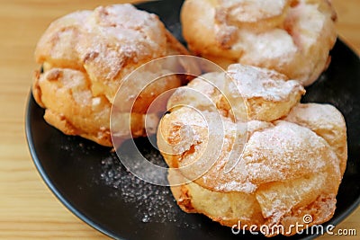 Closeup French Cream Puffs on Black Plate Sprinkled with Icing Sugar Stock Photo