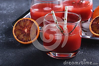 Closeup freshly squeezed juice from red oranges in glasses with tubes on gray background Stock Photo