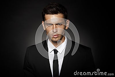 Closeup front portrait of a handsome confident businessman wearing suit standing isolated over black background. Stock Photo