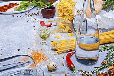 Closeup of a gray table with pasta, glass bottle, red chili pepper, quail eggs and walnuts on a gray background. Stock Photo