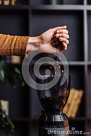 Closeup of the hand of a girl who pours out coffee beans into a black, stylish coffee grinder. Coffee beans slowly fall into the Stock Photo