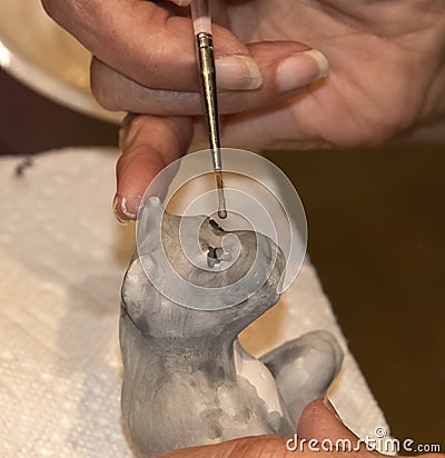 Closeup of hand painting small ceramic animal with paint on tip of brush Editorial Stock Photo