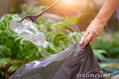 Closeup of hand and waste grabber picking up drinking plastic bottle waste into bag. Ecology and Environmental concerns. Recycling Stock Photo
