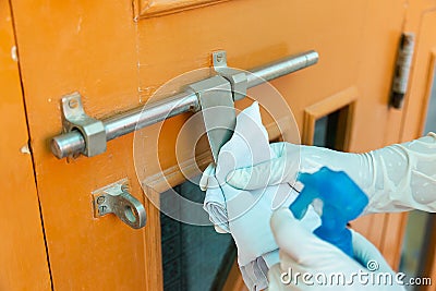 Closeup Of Hand Wearing Protective Gloves cleaning and disinfecting / sanitizing door handles during coronavirus epidemic. Stock Photo