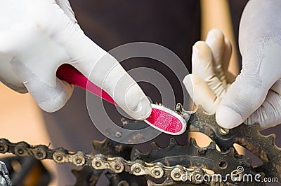 Closeup hand wearing white glove holding toothbrush rubbing on metal bicycle chain, mechanical repair concept Stock Photo