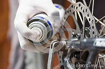 Closeup hand wearing white glove using grease spray on cogwheel parts of bicycle wheel, mechanical repair concept Stock Photo