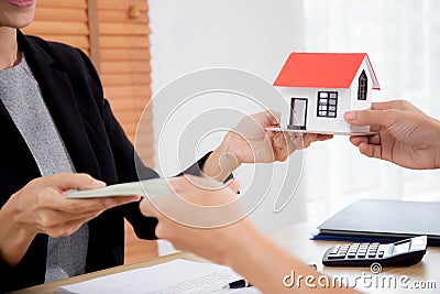 Closeup hand of young realtor woman giving house model to hands customer while client giving money with approval. Stock Photo