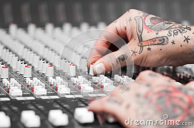 Closeup of hands covered with tattoos working on mixer console, twisting knobs, studio equipment concept