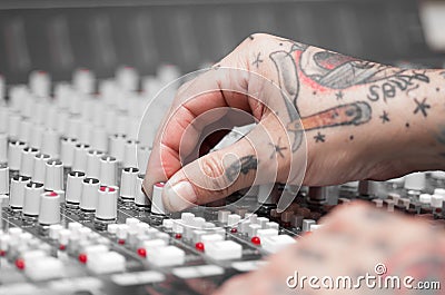 Closeup of hands covered with tattoos working on mixer console, twisting knobs, studio equipment concept