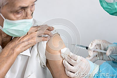 Closeup,Hands of doctor giving Coronavirus vaccine with syringe injection in shoulder of old elderly for prevention COVID-19,asian Stock Photo