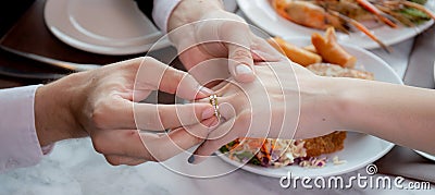 Closeup hands of man putting ring on finger of woman for marriage or engagement together with surprise at restaurant. Stock Photo
