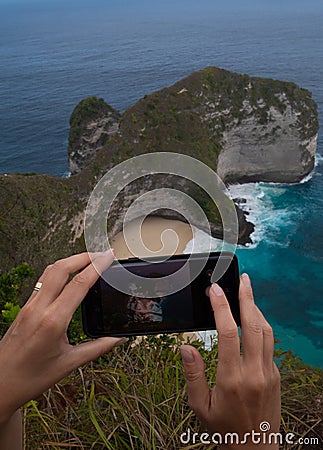 Closeup hands with mobile phone doing photo of Kelingking Beach cliffs in Nusa Penida, Bali Stock Photo