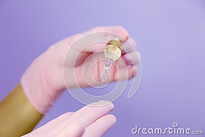 Closeup of hands in pink gloves with pipette and drop of transparent oil Stock Photo