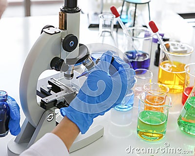 Closeup hands of scientist holding blue reagent dropper working on microscope Stock Photo