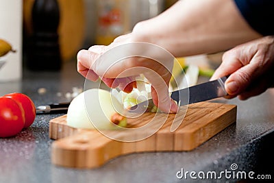 Closeup of the hands of a woman cook slicing onion on a wooden board. Stock Photo