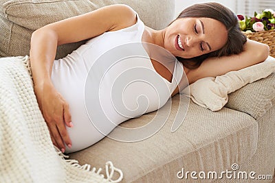 Happy expectant embracing belly on sofa Stock Photo