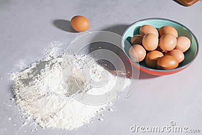 Closeup of a heap of wheat flour next to a bowl filled with brown eggs on a table Stock Photo