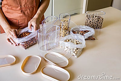 Closeup housewife hands placing nuts plastic package into container box on wooden table at kitchen Stock Photo