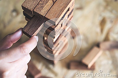 A hand holding and playing Jenga or Tumble tower wooden block game Stock Photo