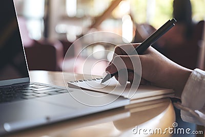 Hand writing down on a blank notebook with laptop on wooden table Stock Photo