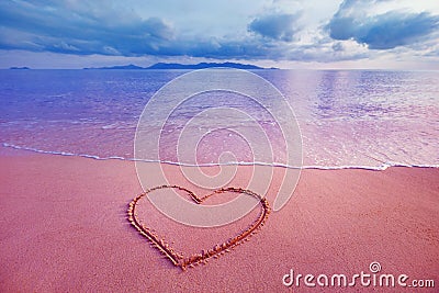 Closeup image of heart symbol written on sand at pink sunrise Stock Photo